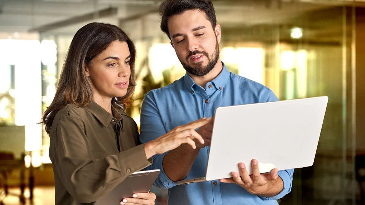 Two workers look at a laptop