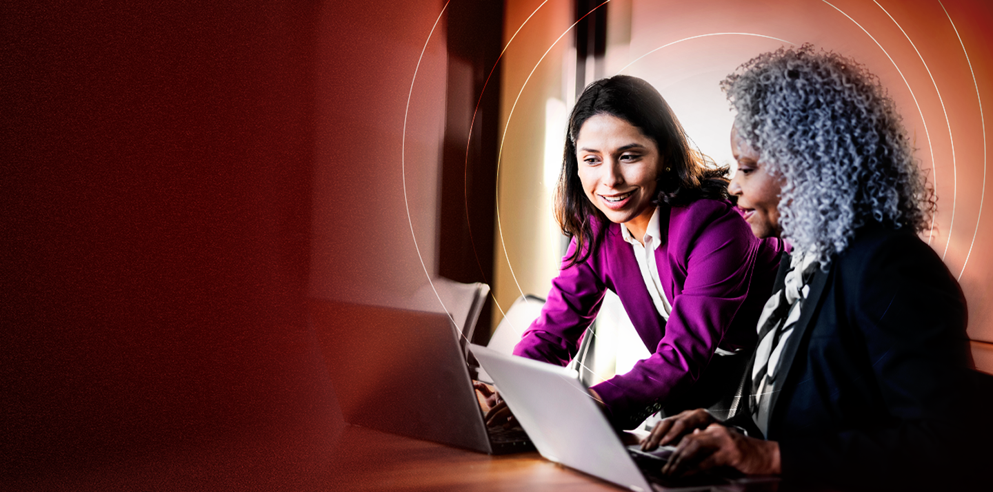 Lady in purple blazer showing something to another employee on latop screen