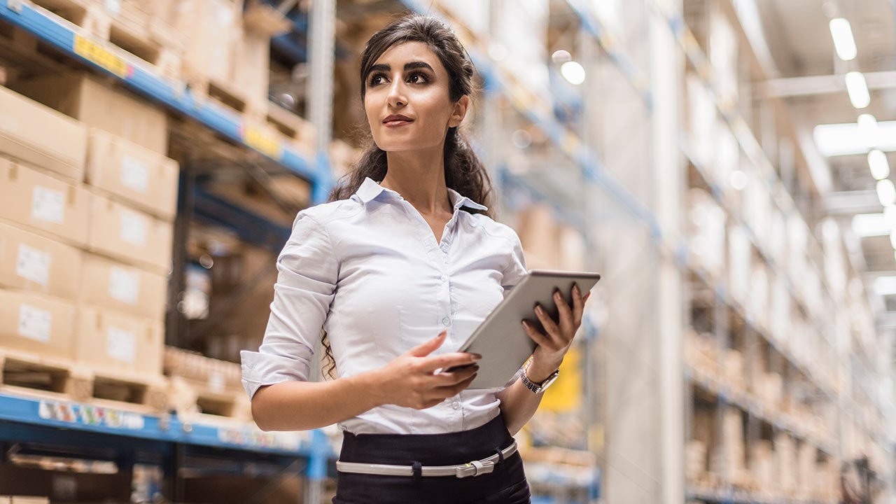 Woman with tablet in factory storehouse looking around.