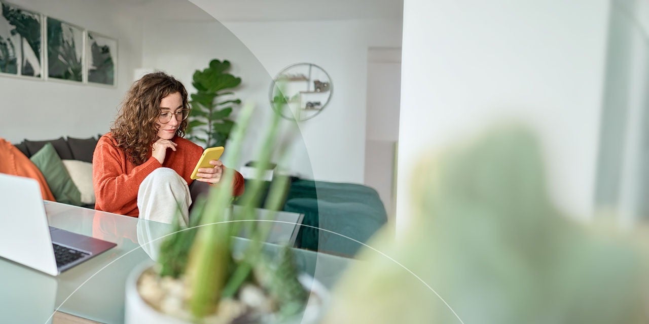 אישה צעירה מחייכת, חובשת משקפיים אוחזת בסמארטפון.