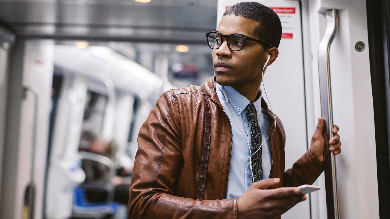 Man on the tube with headphones holding iphone