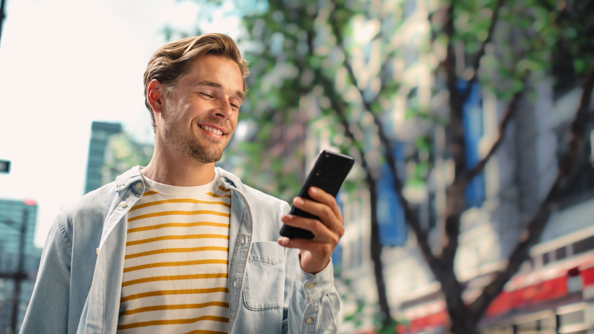 Muškarac šeta ulicom i gleda u mobilni telefon. 