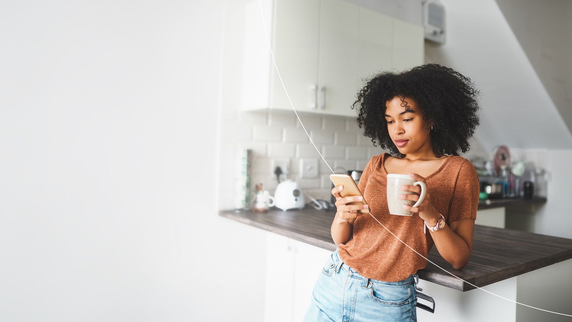 woman with coffee cup using phone in the kitchen.