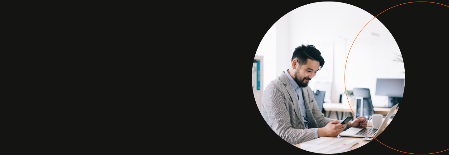 Man working on a laptop with his phone in an open concept office