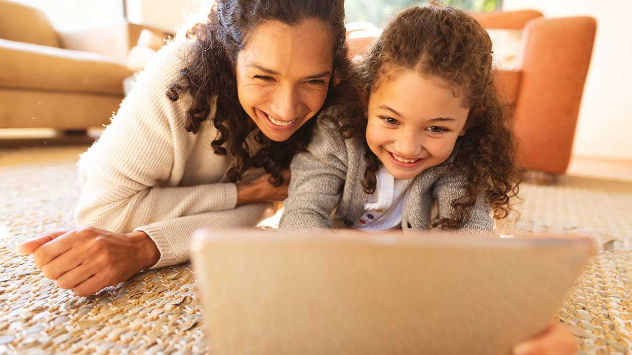 En kvinde og en pige ligger på gulvet og kigger på en bærbar computer.