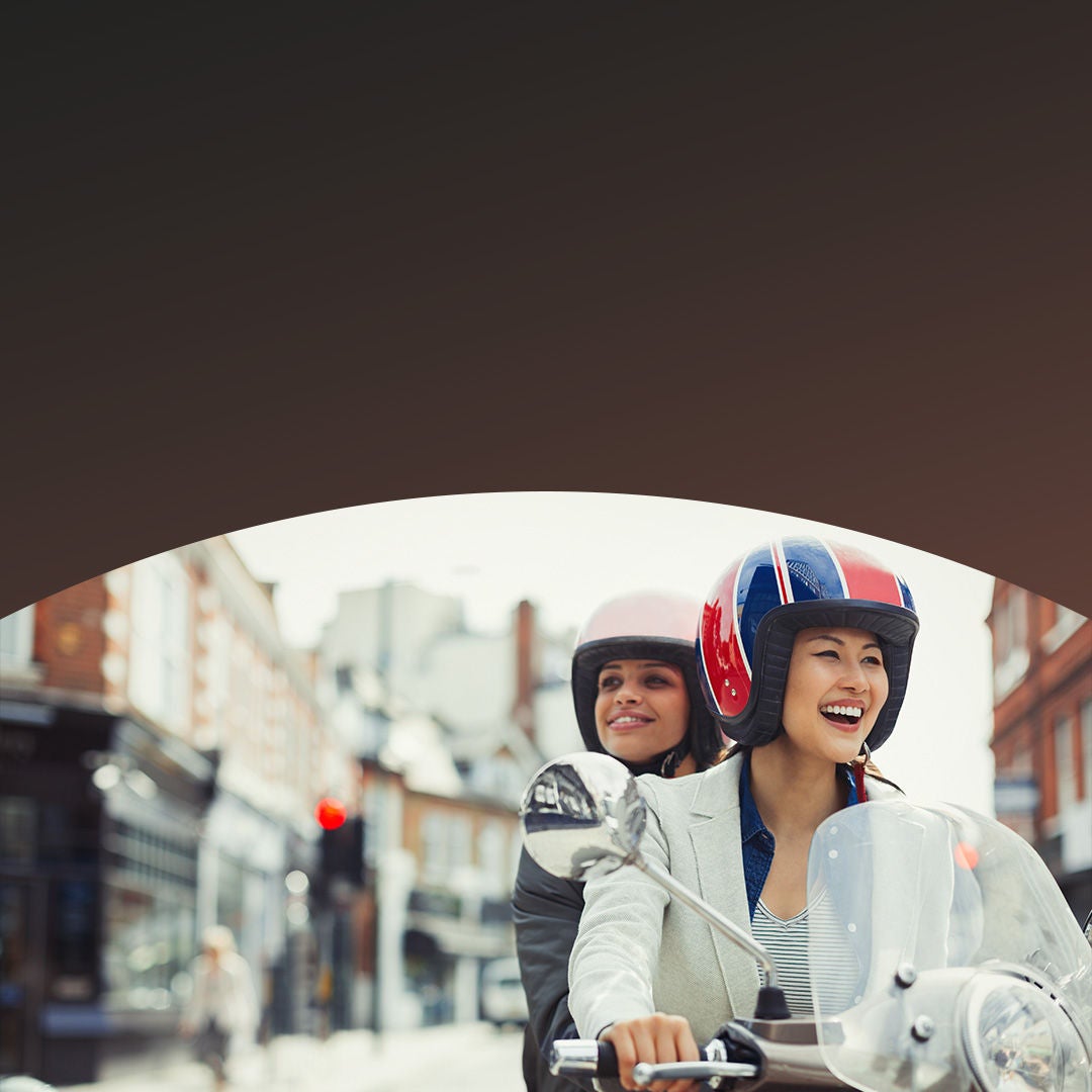 Two women riding scooter in street.