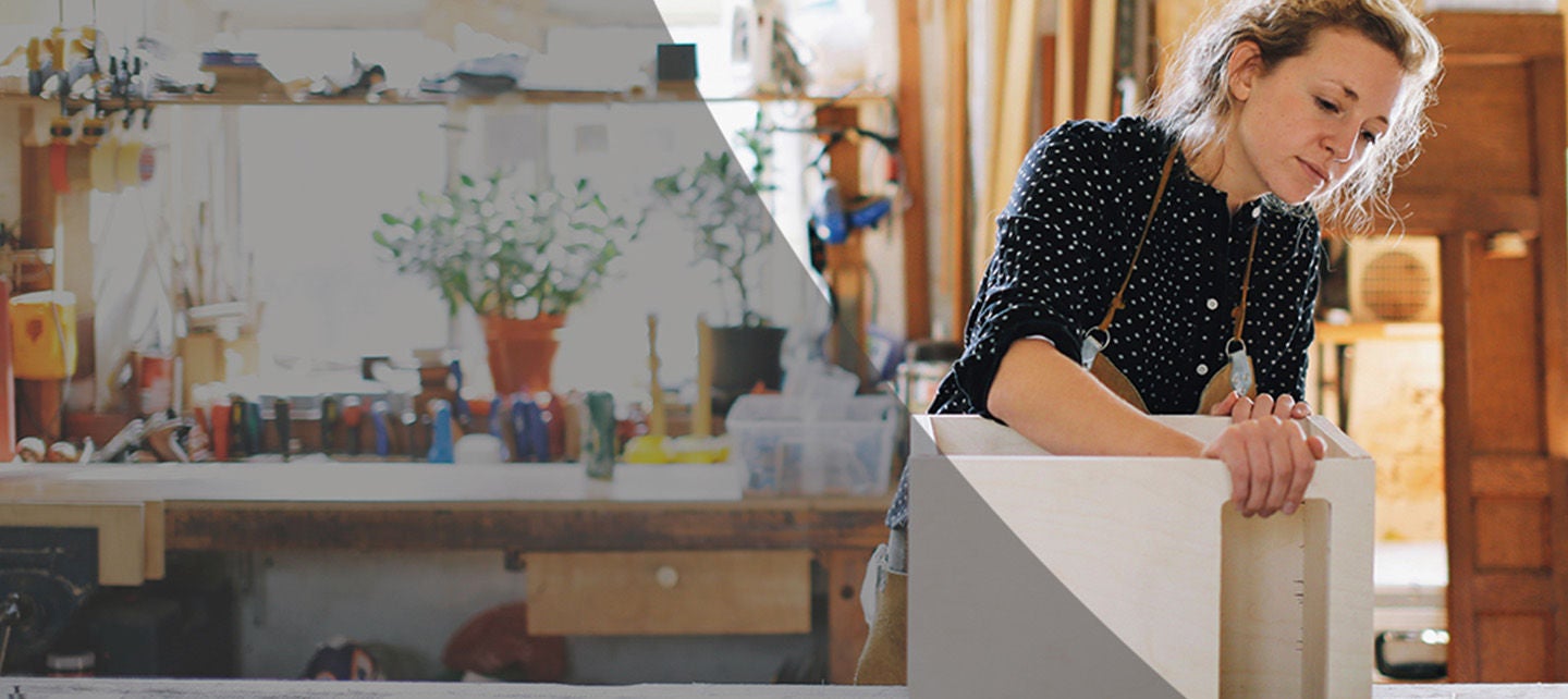 En person arbeider med treverk i verkstedmiljø, omgitt av verktøy og materialer.