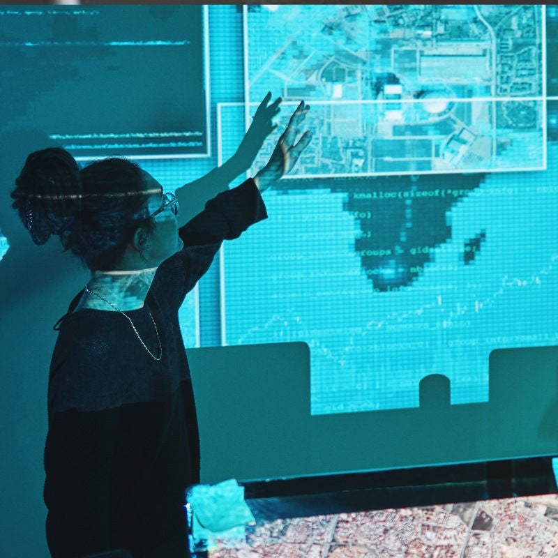 A cyber analyst points to a projected map on a wall. 