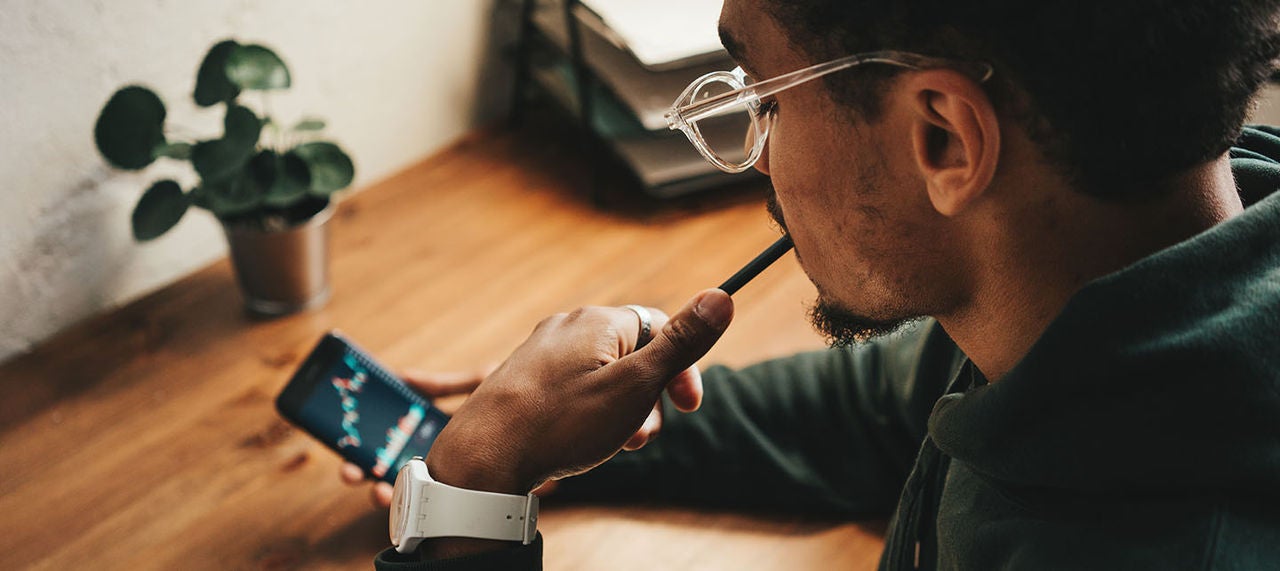 Young man sitting at desk reviewing financial charts on his smartphone.