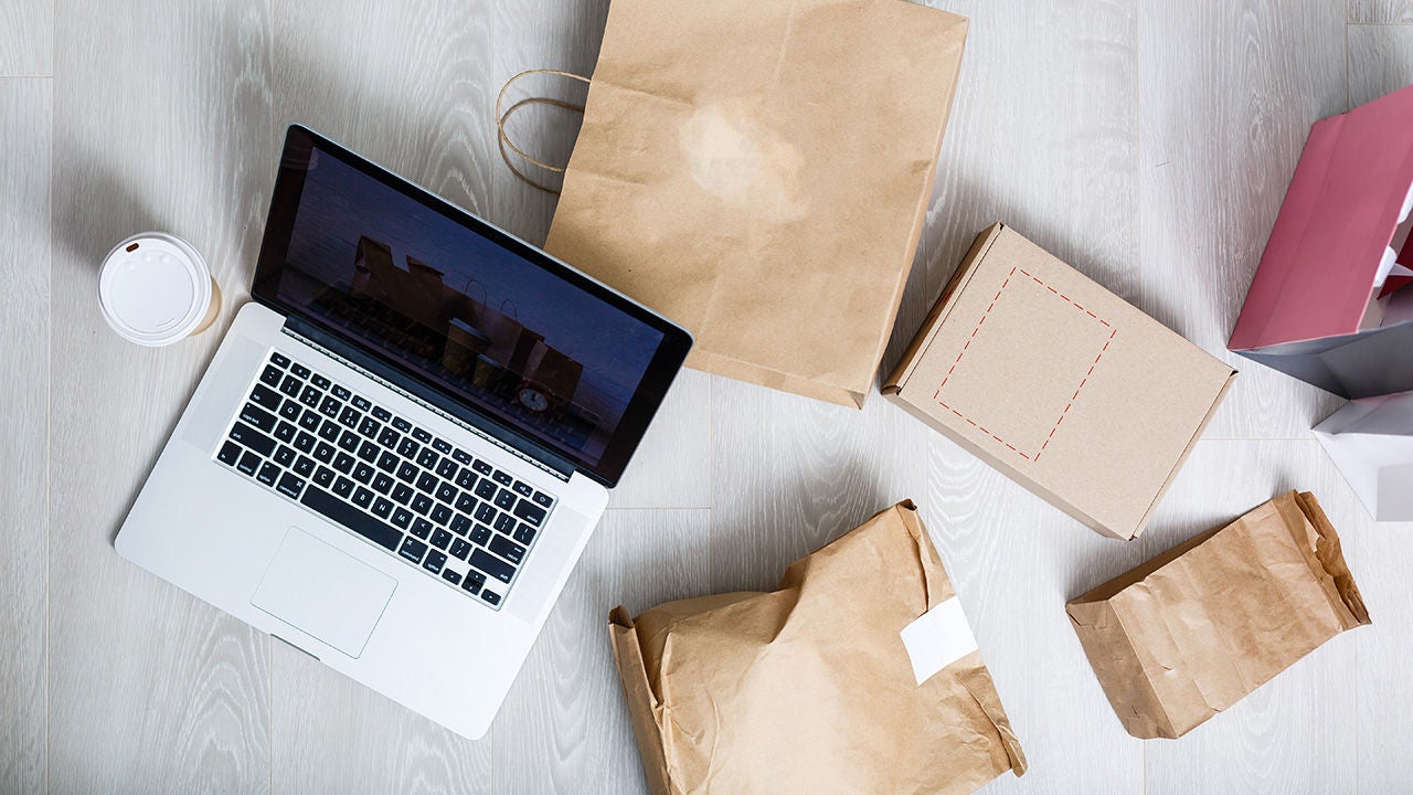 Laptop auf einem Tisch mit Papiertüten und Kartons.