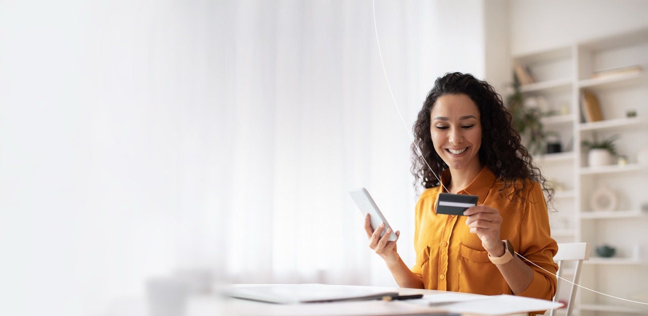 woman sitting at table holding her phone and looking at her credit card.
