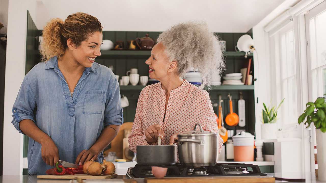 To kvinder laver mad sammen i et køkken og smiler til hinanden.