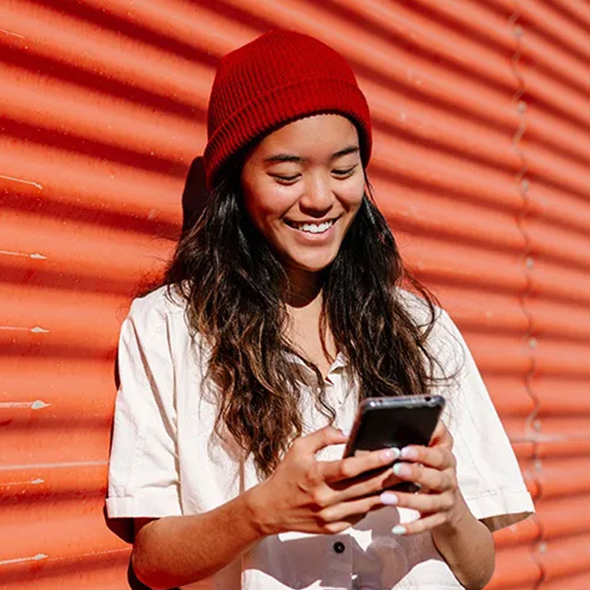 Woman smiling at her phone in front of an orange wall.