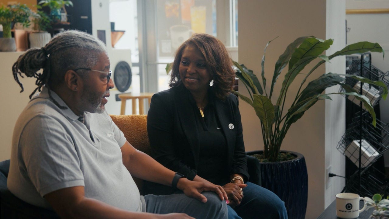 The owners of Momentum Coffee sitting on chairs and talking. 