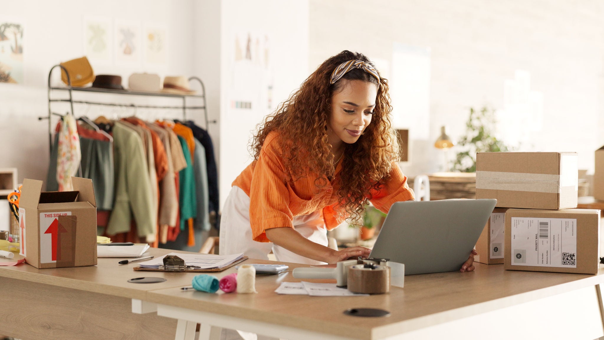 Junge Unternehmerin arbeitet am Laptop und bereitet Pakete für den Versand für ihr Online-Kleinunternehmen vor.