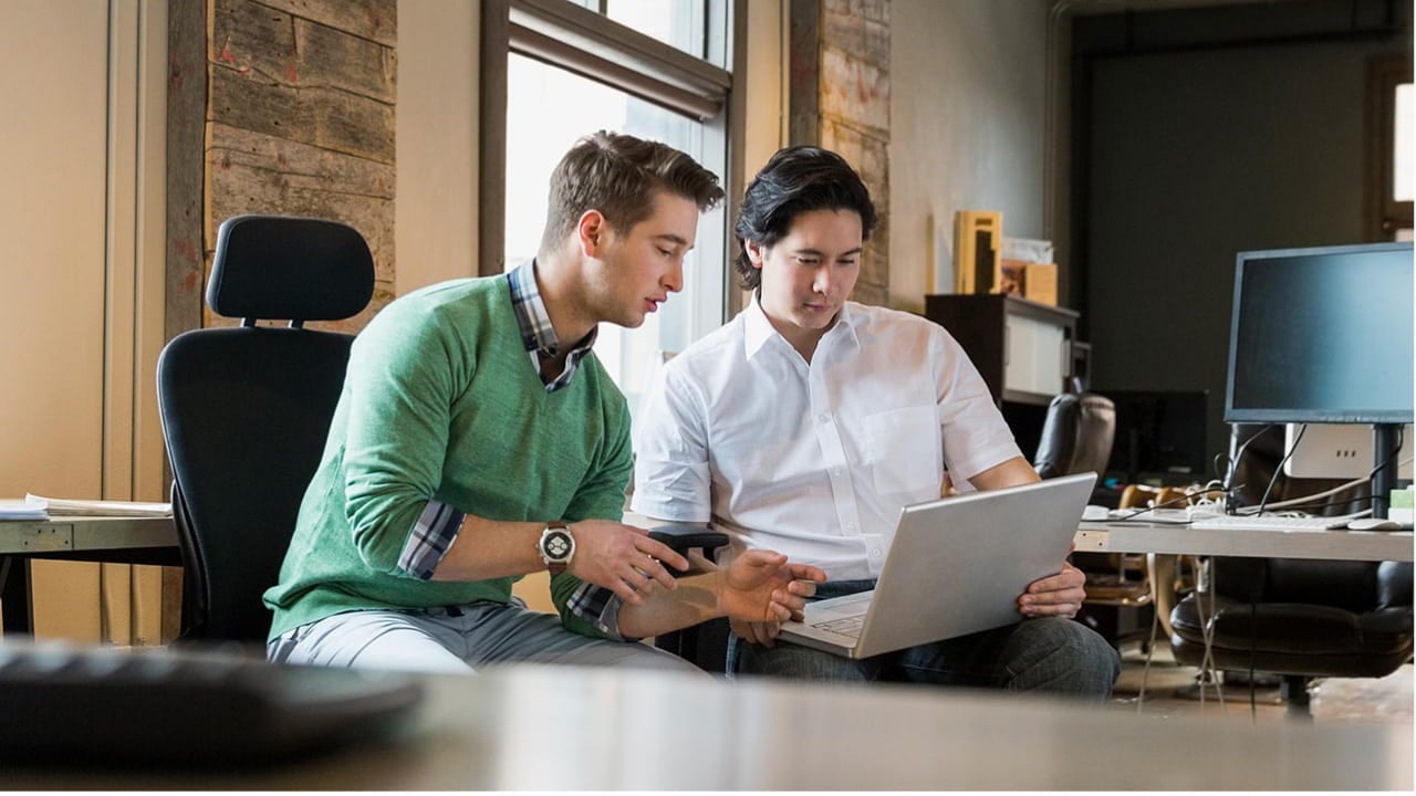 two men collaborating on laptop at a desk