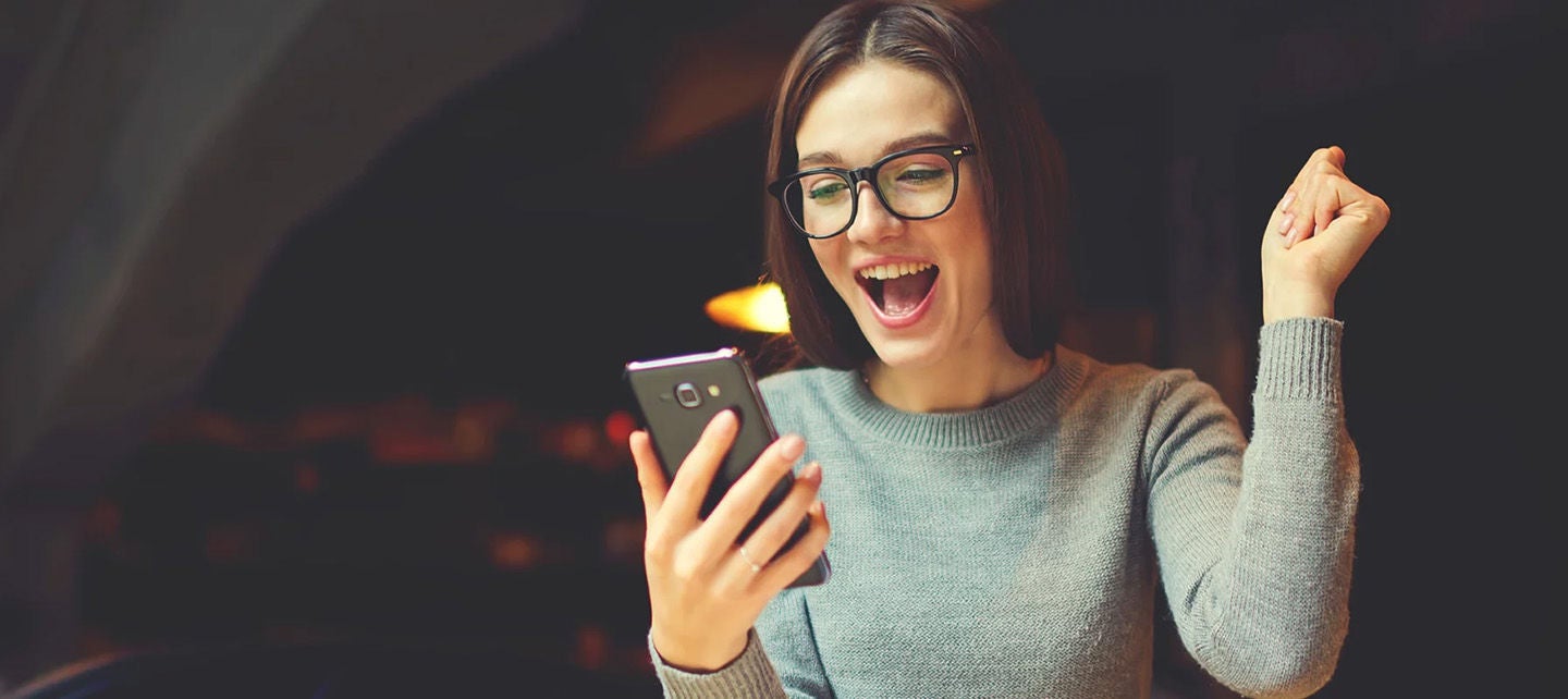 Frau schaut mit aufgeregtem Gesichtsausdruck auf ihr Handy