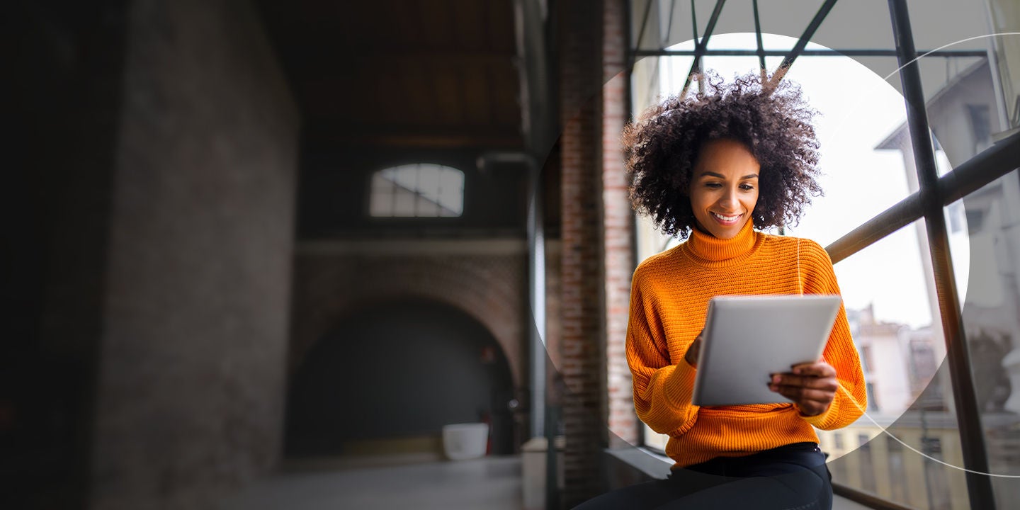 woman in orange sweater holding a tablet.