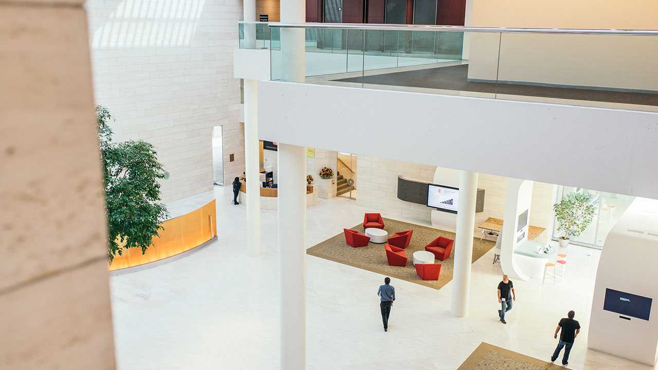 En moderne og lys lobby med hvide vægge, røde lænestole og flere personer, der bevæger sig rundt i rummet.