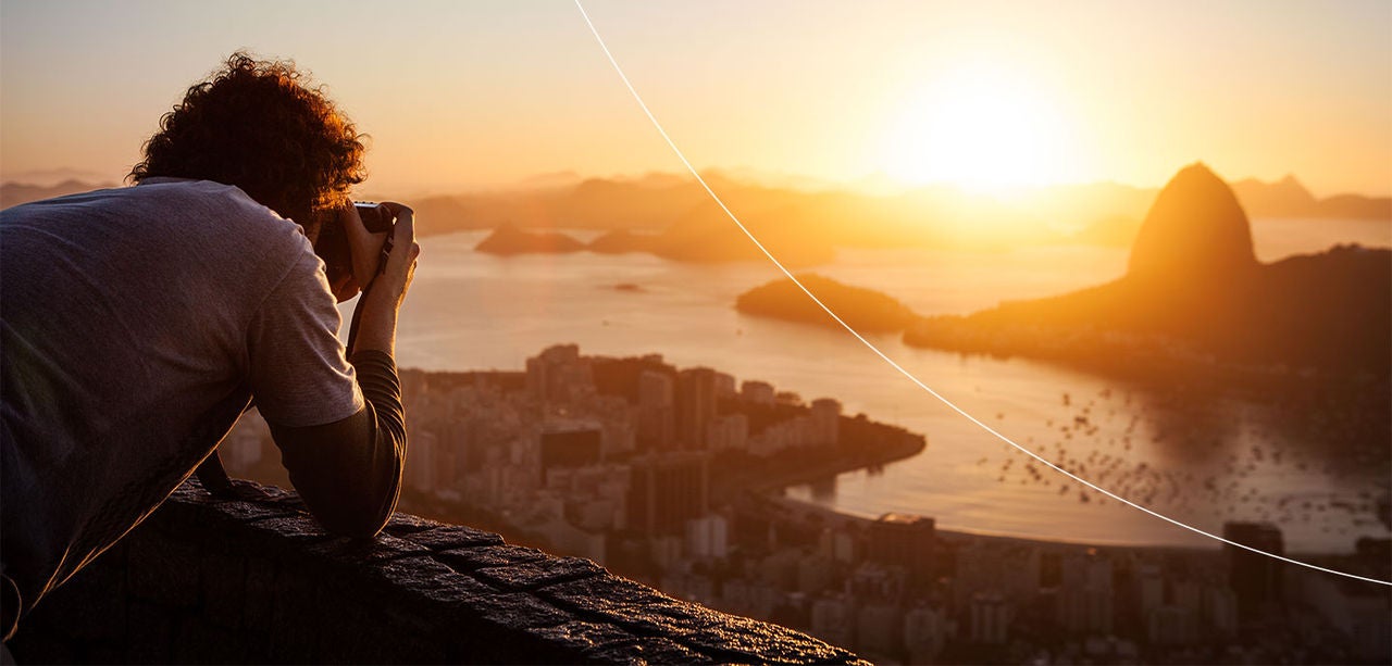 En person fotograferer en by og en solnedgang over havet.