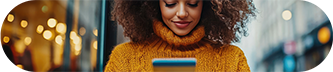 A woman with curly hair gazes her phone, focused on the screen. 