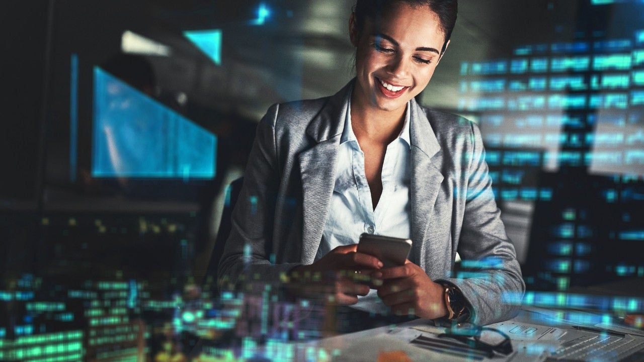 A woman locks at her phone at night in an office. 