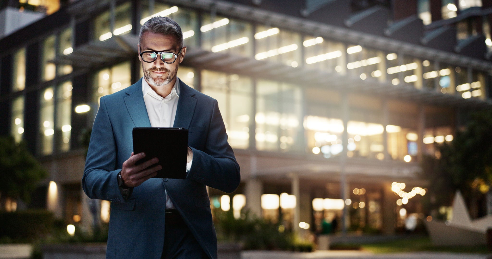 Mature businessman, tablet and building at night for office innovation, research and company regulations in city. Male boss, smile and tech in evening for info, update and report for accounting firm.