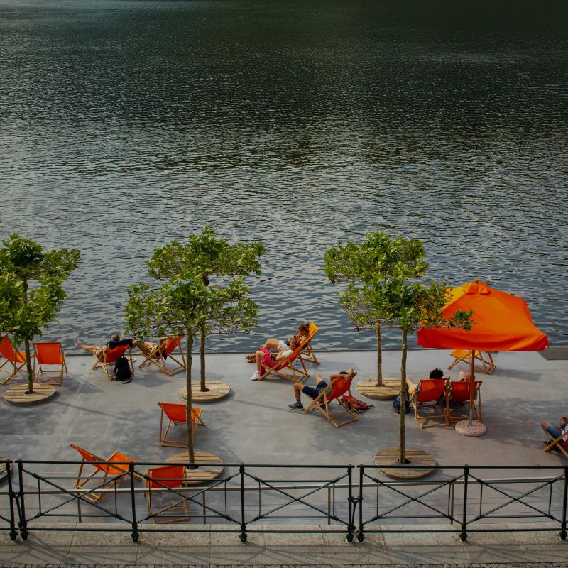 People sit on orange chairs on a large patio overlooking a lake. 