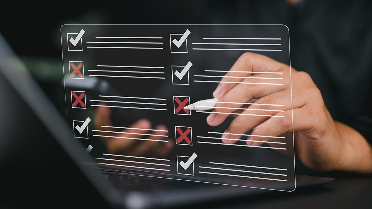 Hands checking off list overlay in front of laptop.