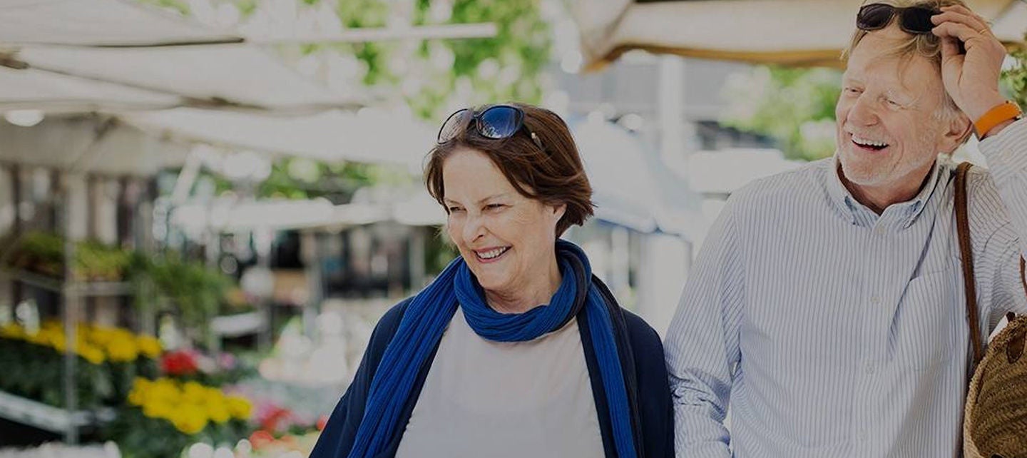 Två personer går utomhus och ler, med blommor i bakgrunden.