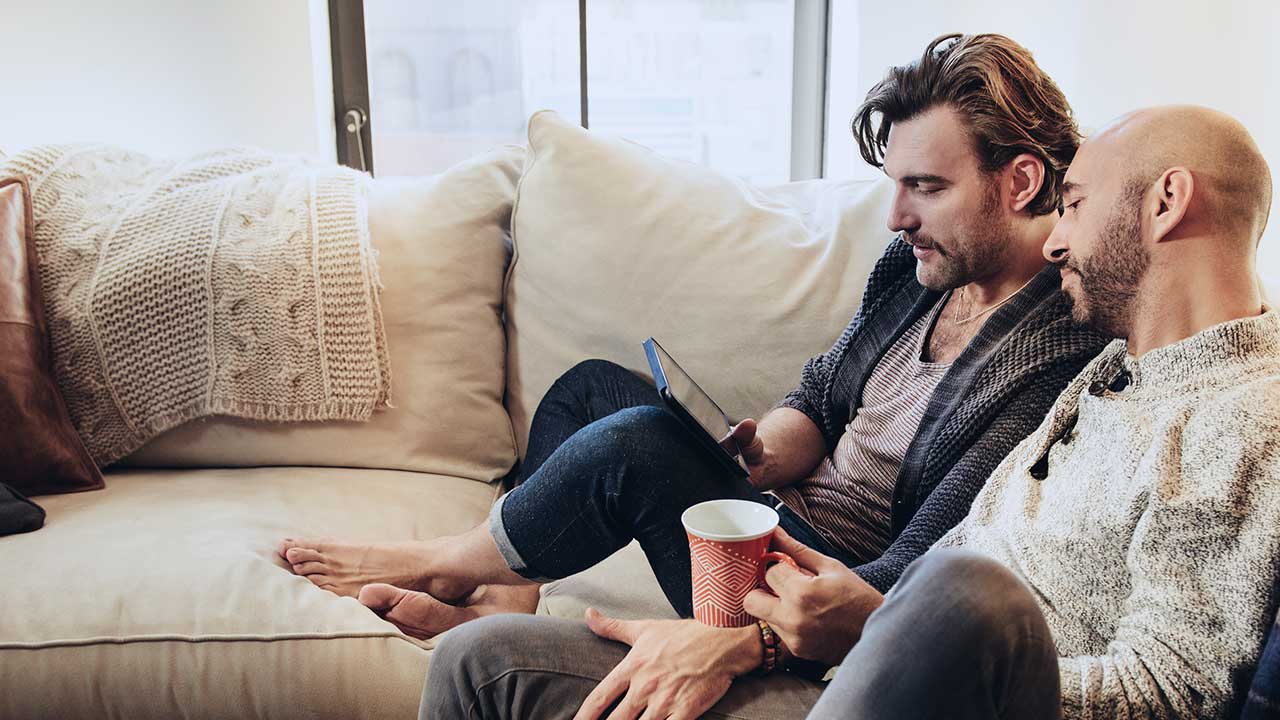 Two men sitting on a sofa looking at a tablet to view different card options.