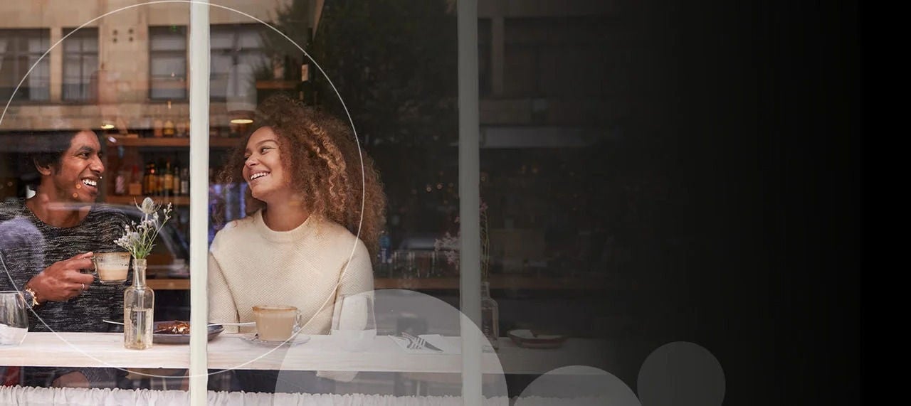 אישה מחייכת ומביטה במישהו שלידה, הפונה אל החלון.