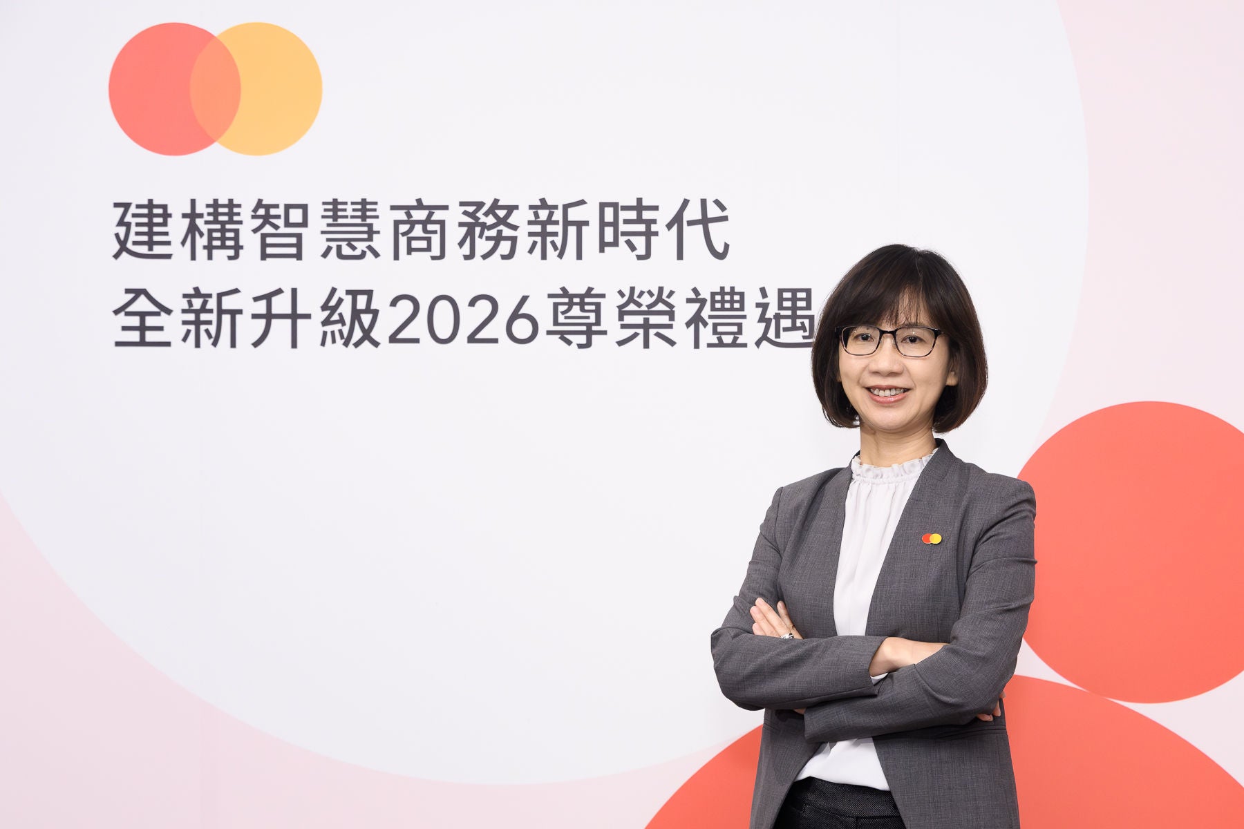 A woman in a grey blazer stands with her arms crossed, smiling in front of a white backdrop with Chinese text and a brand logo.