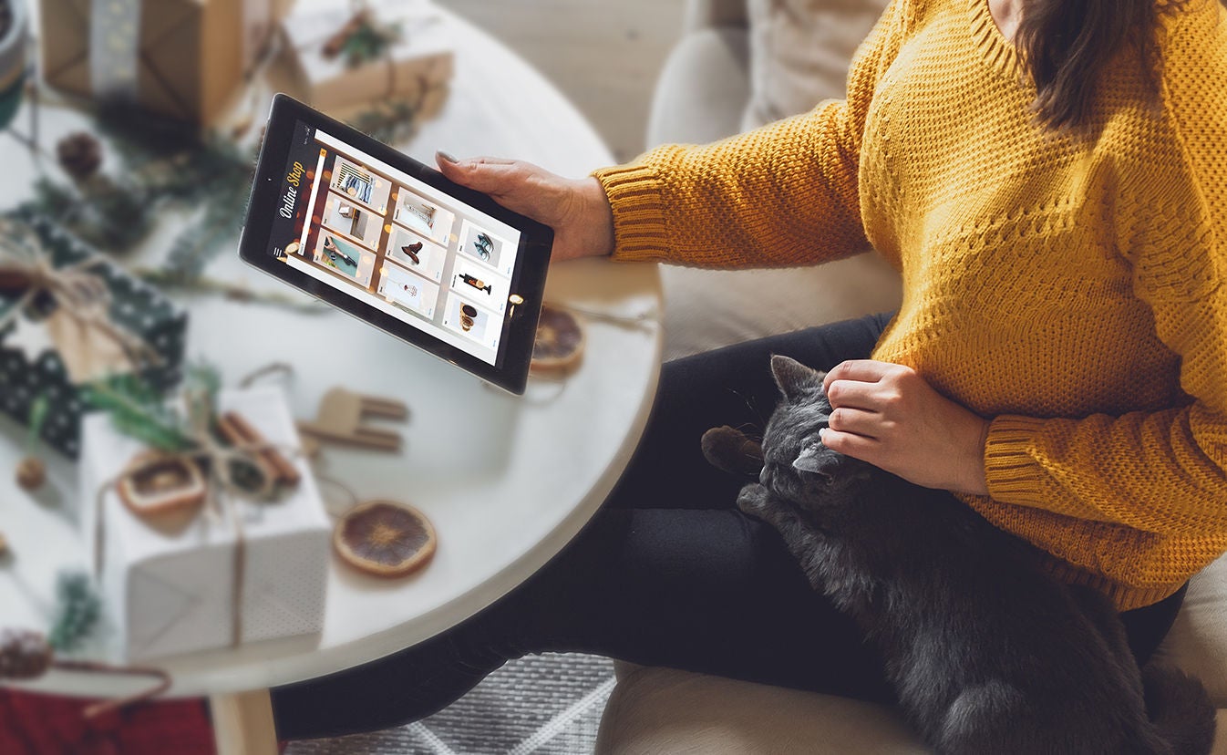 Woman petting her cat and christmas shopping on a tablet.