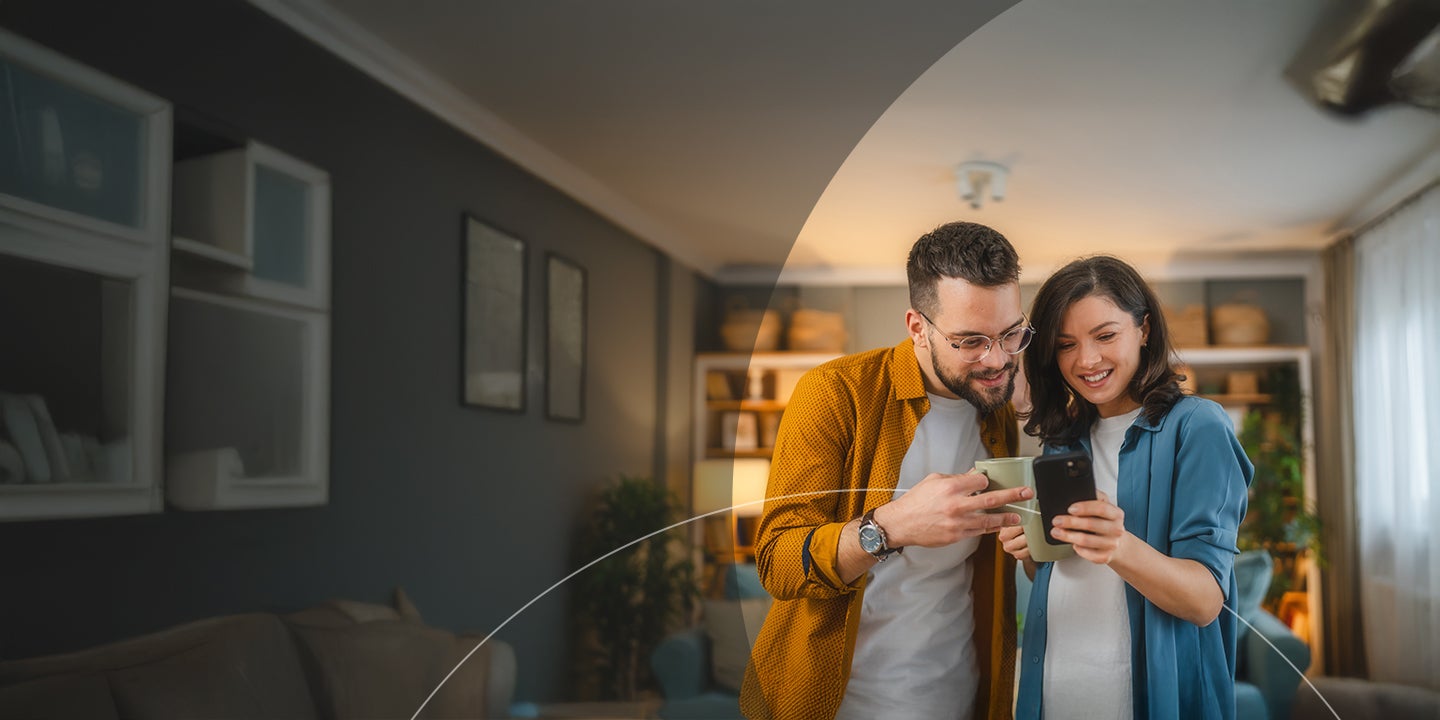 Happy husband and wife having a cup of coffee while using mobile phone.