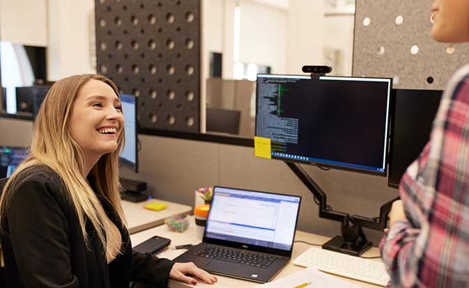 Woman smiling while looking at a laptop with a coworker nearby.