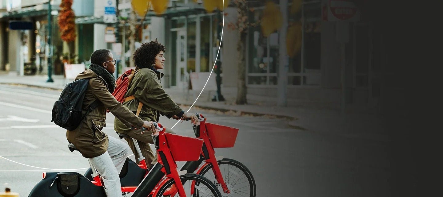 שני אנשים עם תרמילים רוכבים על אופניים אדומים ברחוב עירוני.