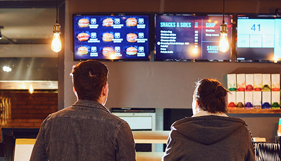 Zwei Männer schauen sich die digitale Speisekarte in einem Fast-Food-Restaurant an.