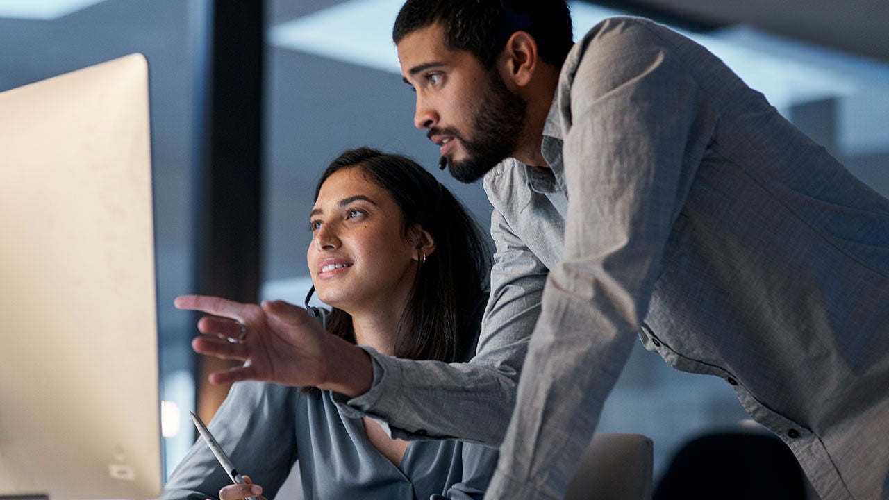 Young man helping his colleague in a call centre late at night.
