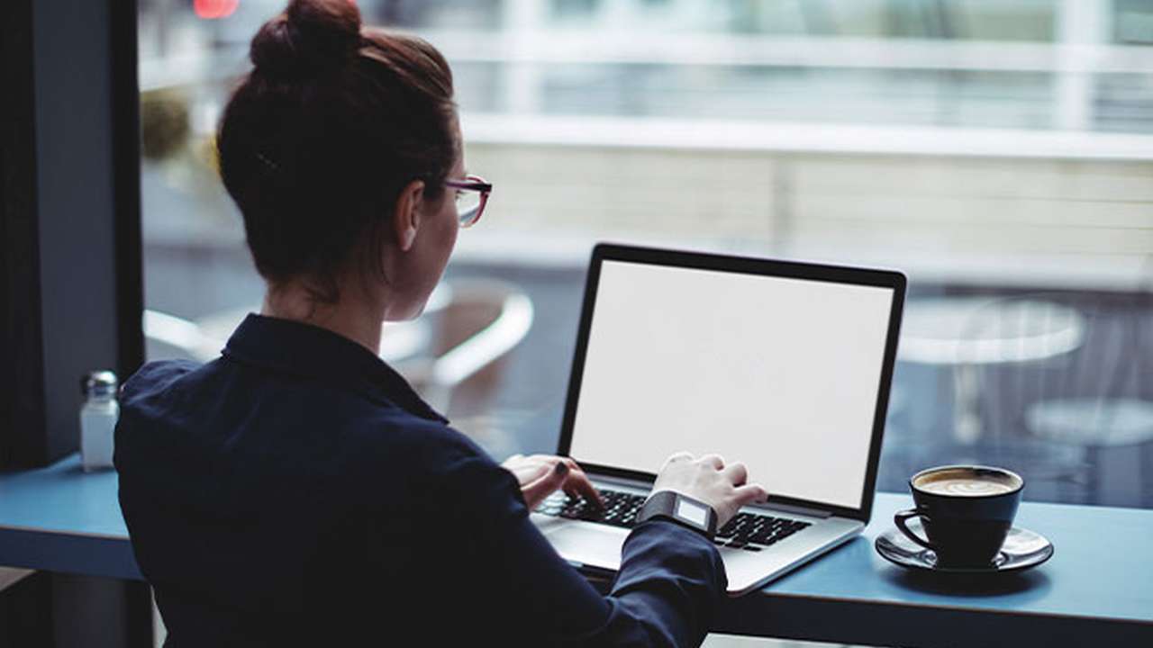 En kvinde, set bagfra, arbejder på sin bærbare computer på en café.