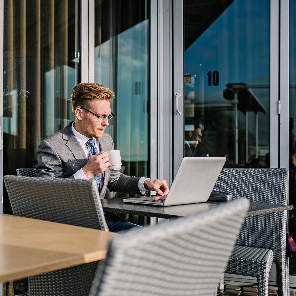Man in a suit working on a laptop outdoors with a coffee.