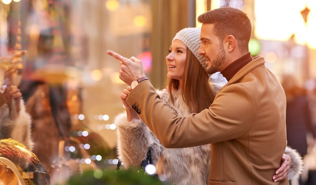 A woman with her hand around a man together look at a window display. 