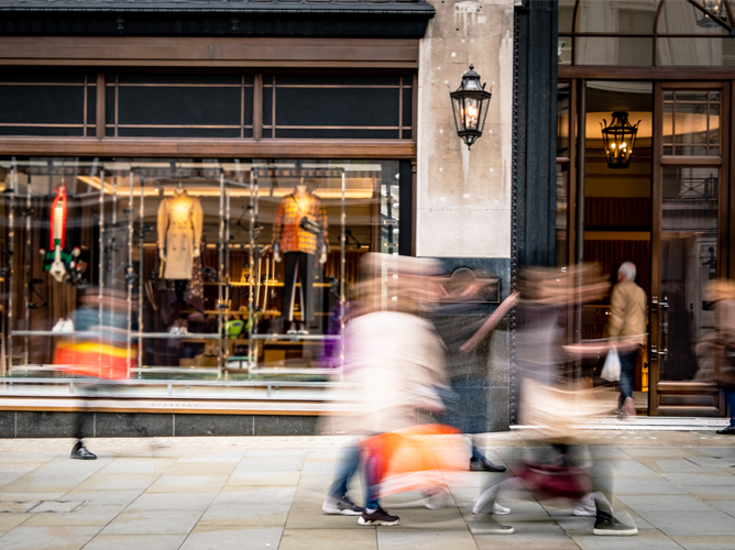 A motion-blurred view of pedestrians walking past a high-end retail store, illustrating a high-low European economy amid inflation.