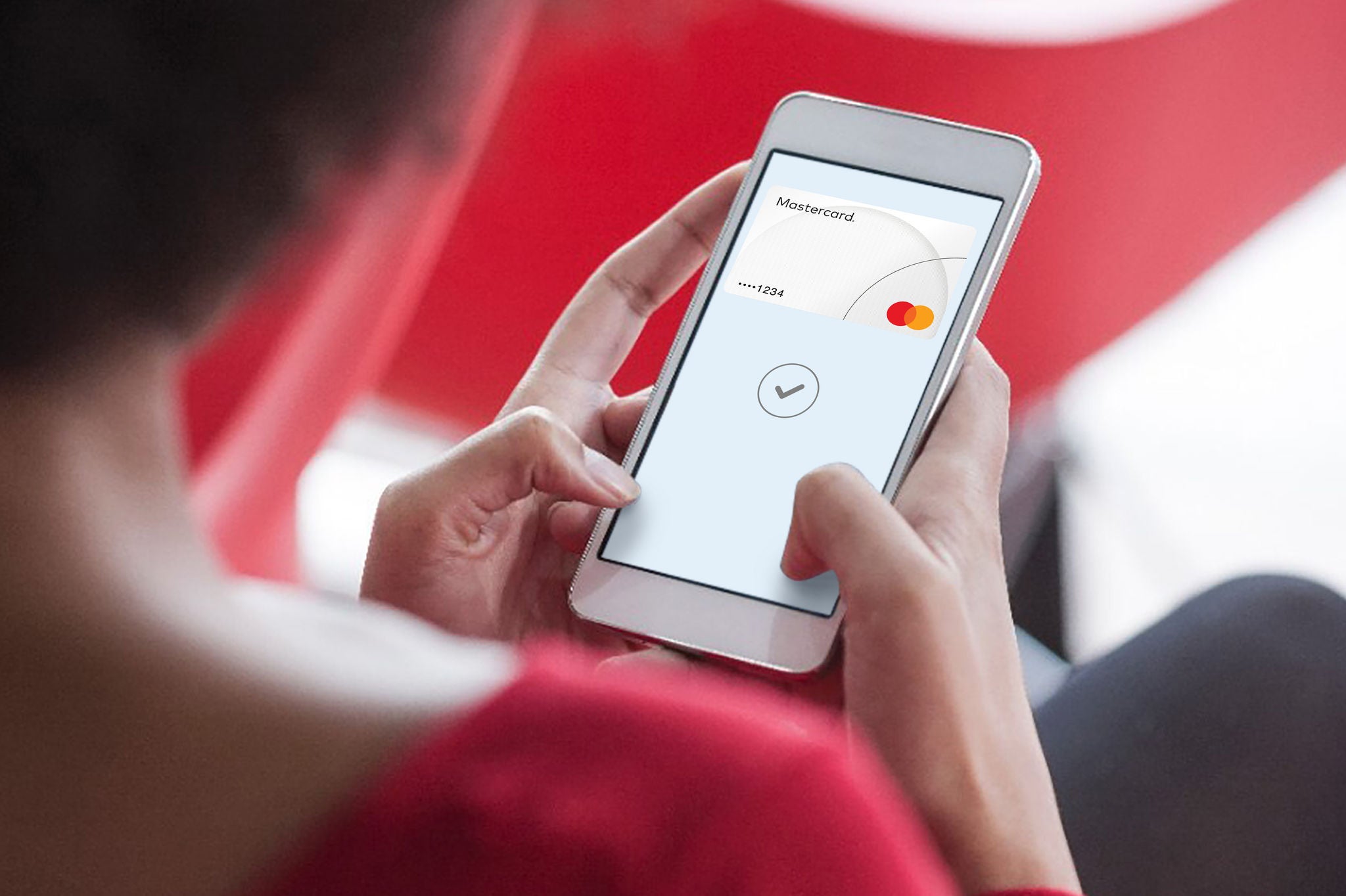 An over-the-shoulder view of a person holding a phone showing a payment card and a checkmark on screen.