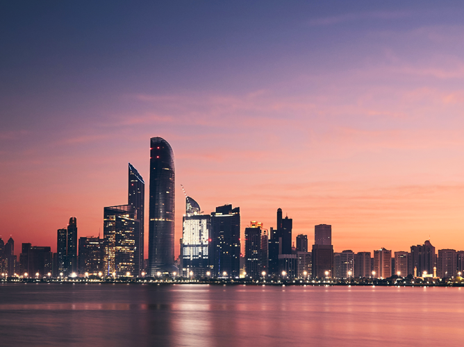The modern Abu Dhabi city skyline at dusk with lights reflecting on the water, showing how tourism fuels economic diversification.