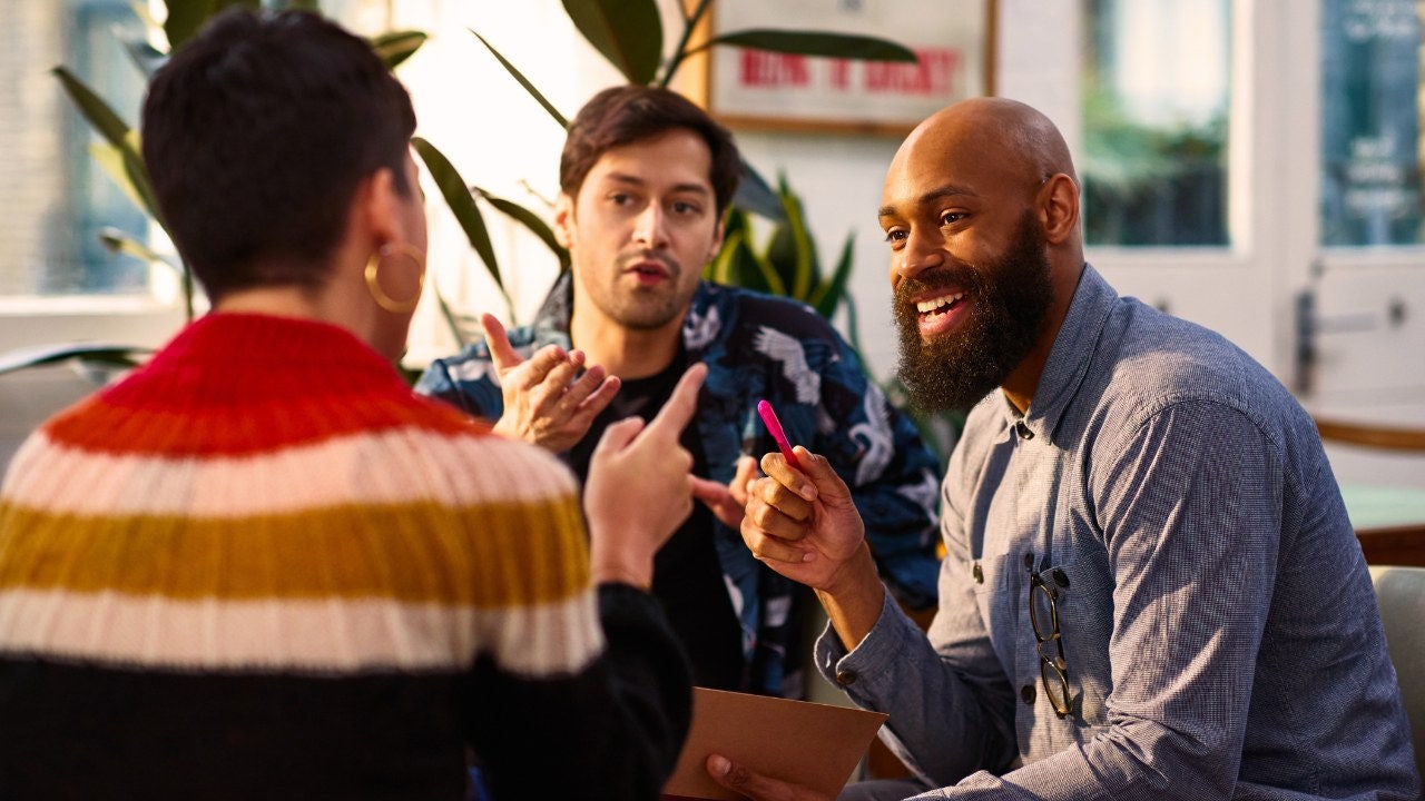 Three colleagues chat animatedly in a casual office. 