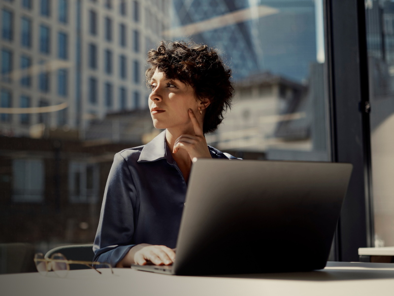 Femme dans un bureau regardant au loin avec un ordinateur portable devant elle