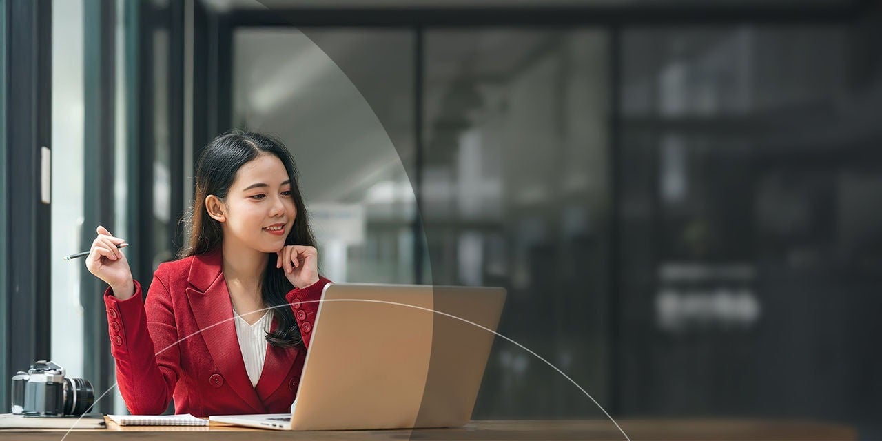امرأة تحمل قلمًا بينما تنظر إلى جهاز الكمبيوتر المحمول في المكتب.