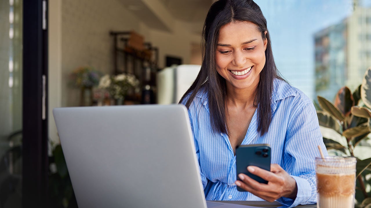 Businesswoman using cellphone and working on laptop while in cafe.