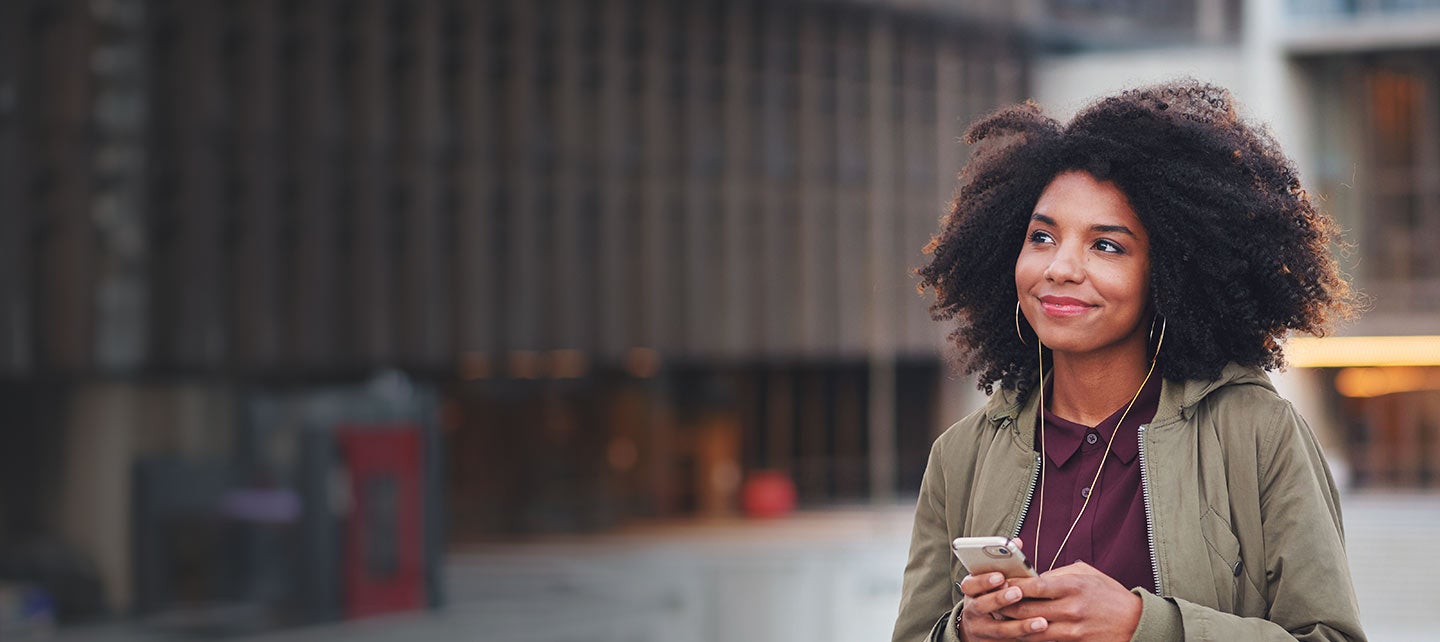 Person with phone and earbuds walking on a street.